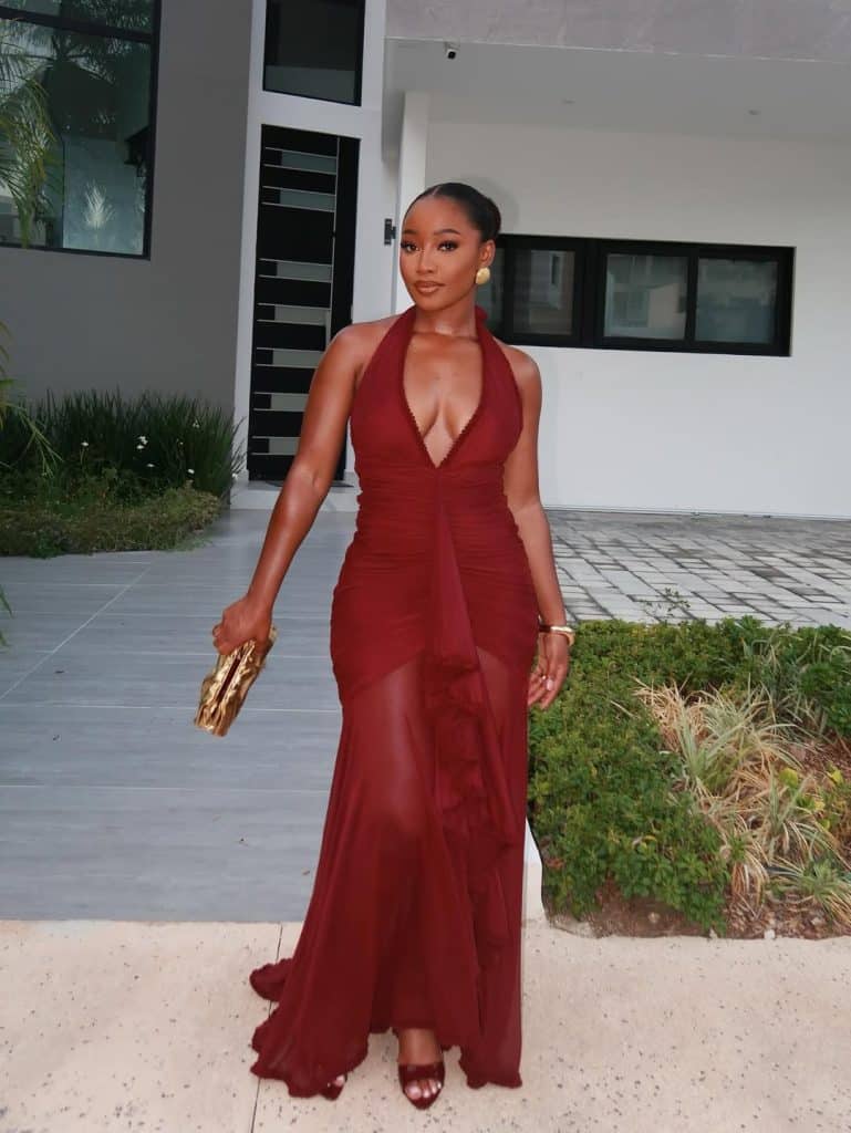 A woman in a burgundy halter-neck gown with ruched detailing and gold jewelry.