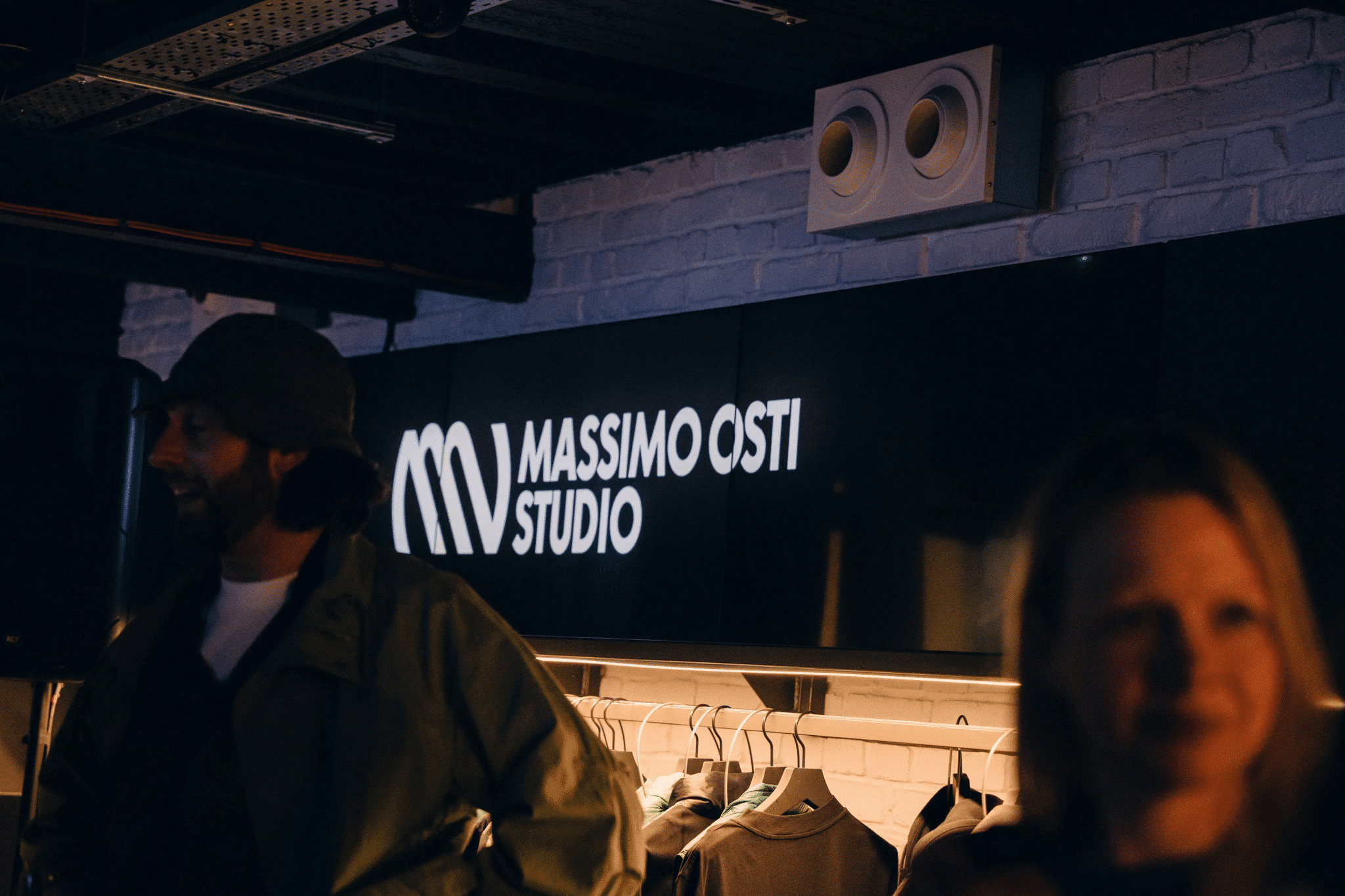Inside a dimly lit Massimo Osti Studio store with neon signage and racks of casual menswear.