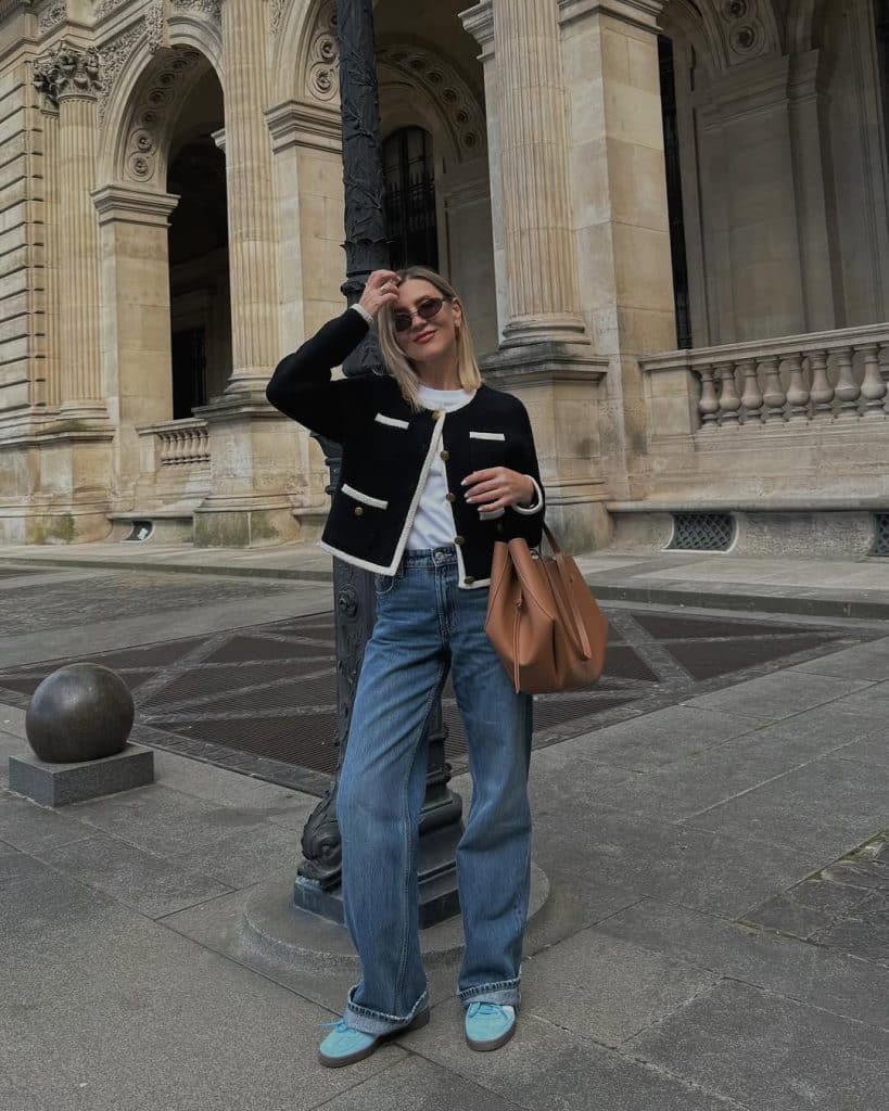 A woman wearing a black tweed cardigan jacket with white trim and wide-leg jeans in front of a stone building.
