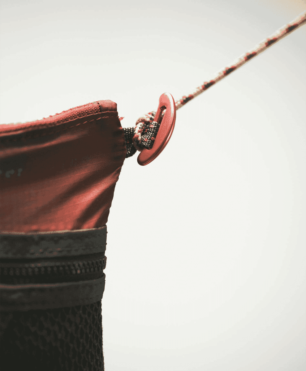 Close-up of a red and black outdoor gear pouch with a metal loop and cord.