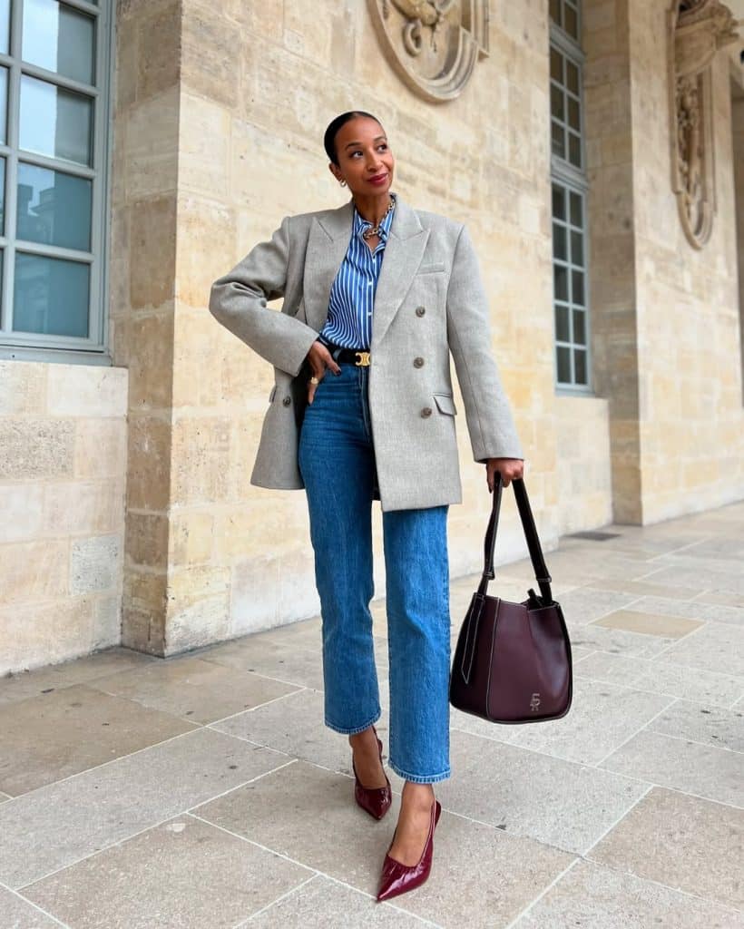 A woman in a gray blazer and striped shirt paired with wide-leg jeans and burgundy heels.