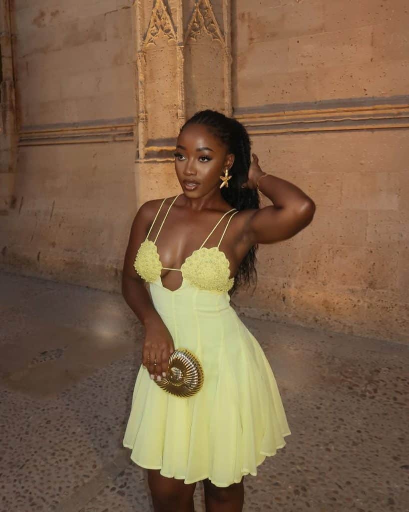 Woman in a yellow mini dress with crochet embellishments and a nautilus clutch.