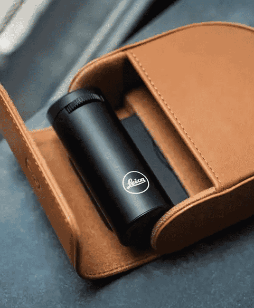 A black Leica accessory in a tan leather case on a blue surface.