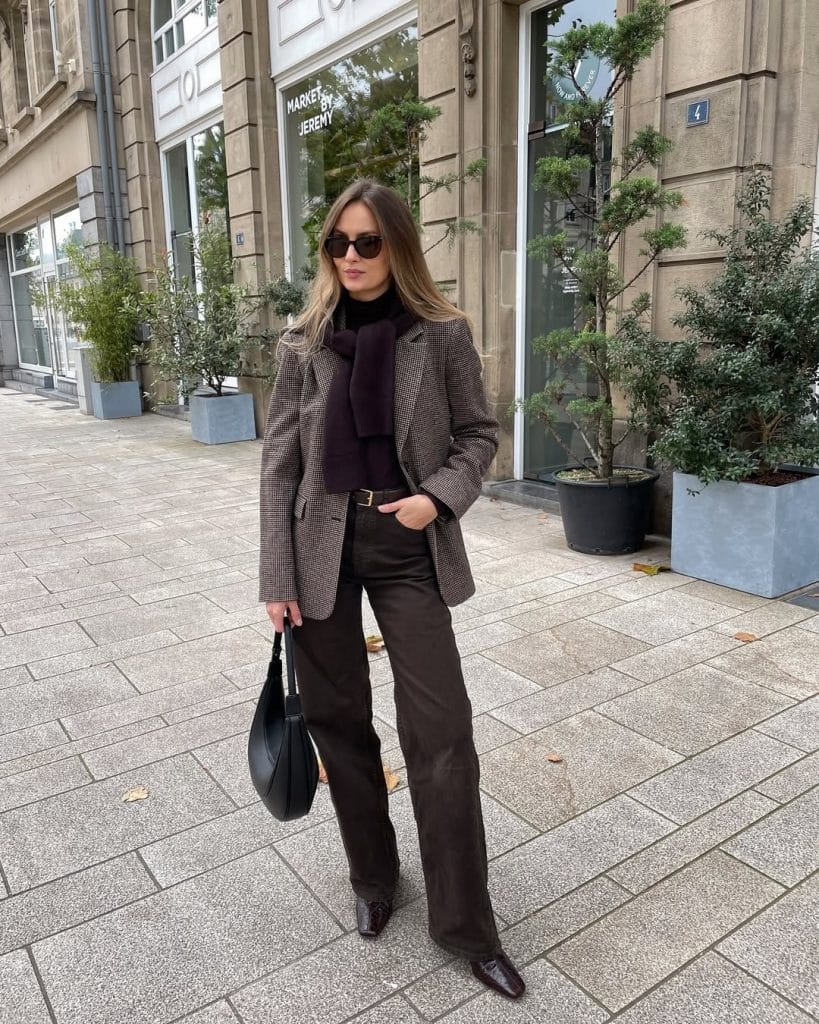 Woman in a houndstooth blazer and dark wide-leg trousers with sunglasses.