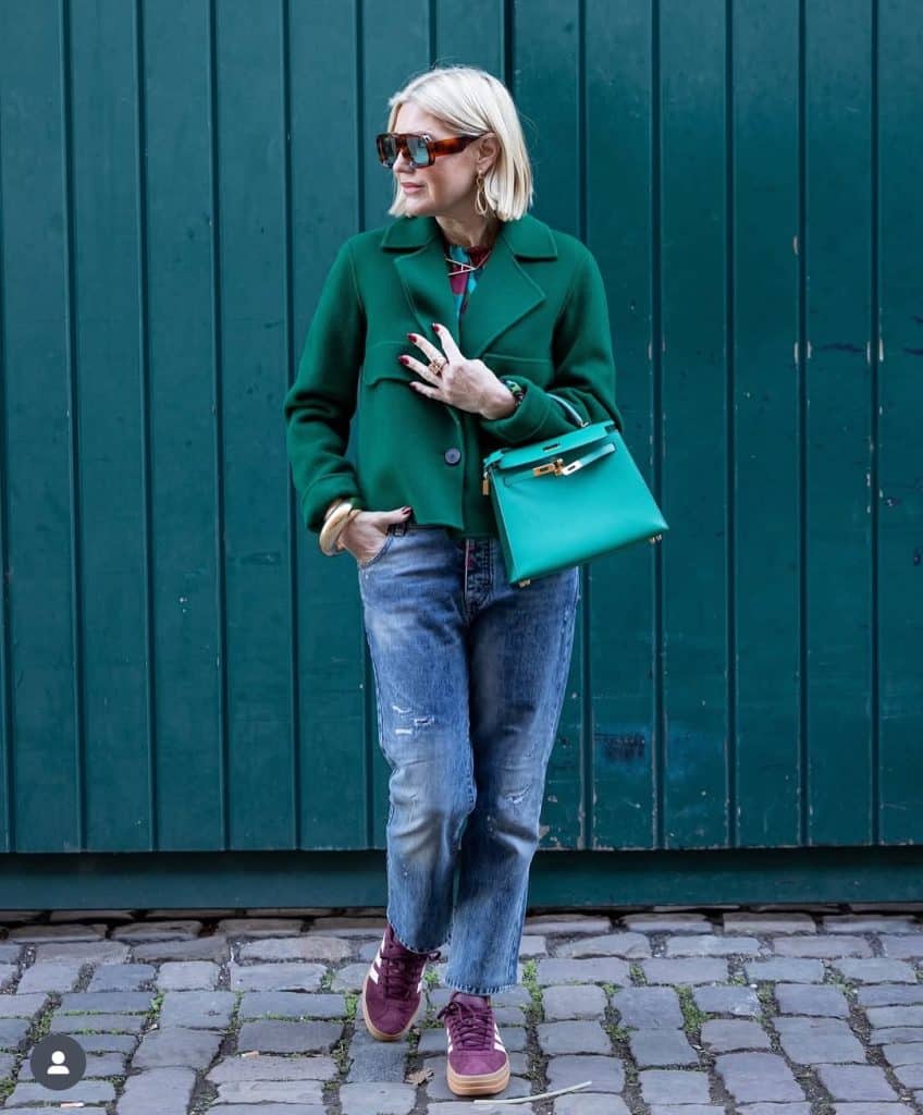 A woman over 50 wearing a vibrant emerald green coat and burgundy sneakers.