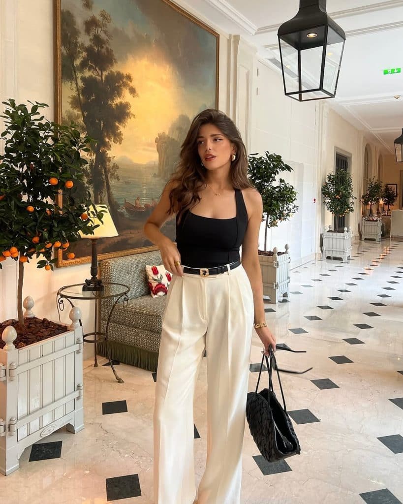 A woman in a black halter top and cream wide-leg trousers posing in a luxury hotel lobby.
