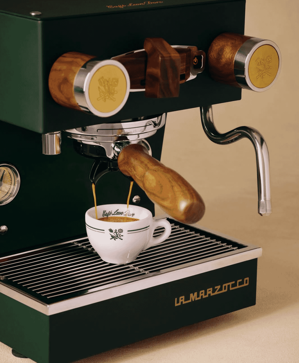 Close-up of the green espresso machine's portafilter pouring espresso into a branded cup.