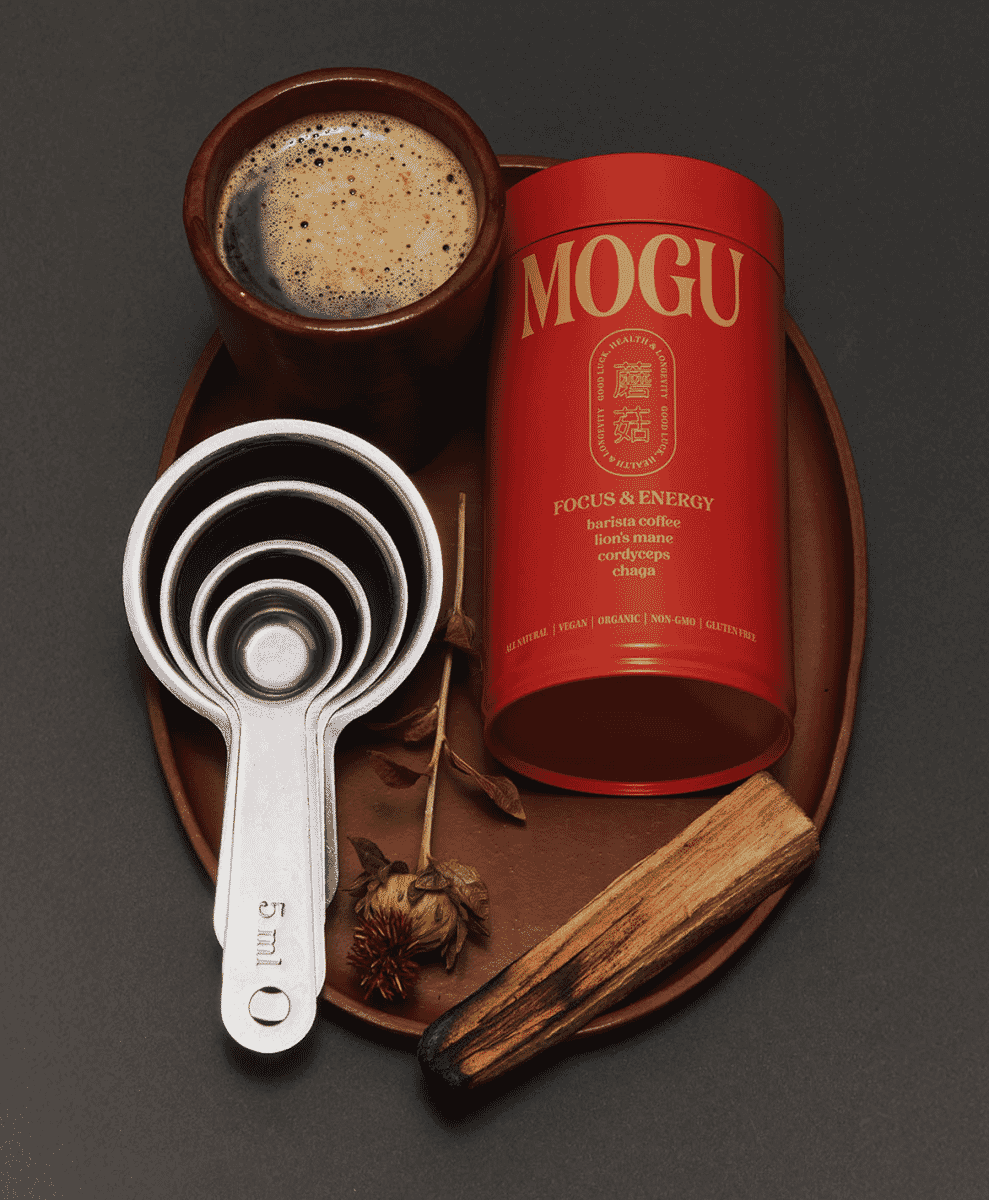 A steaming mug of mushroom cacao on a wooden table next to a book and a soft blanket.