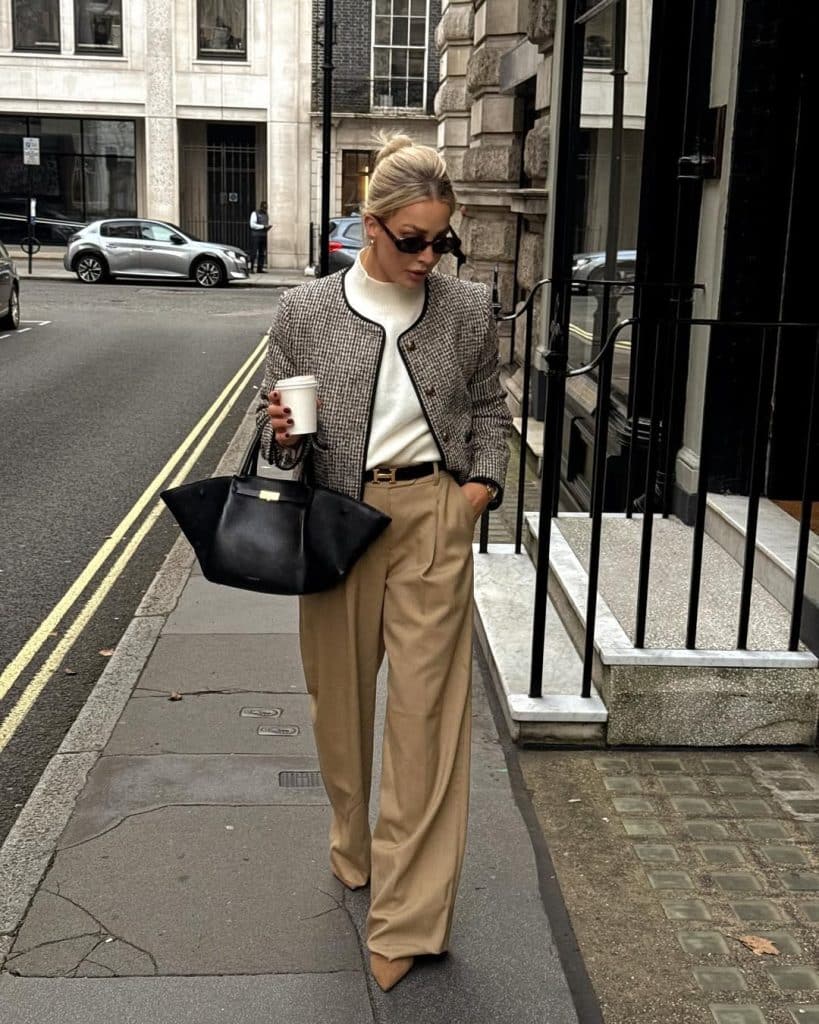 A woman in a camel-toned tweed blazer and wide-leg trousers walking down a city sidewalk.