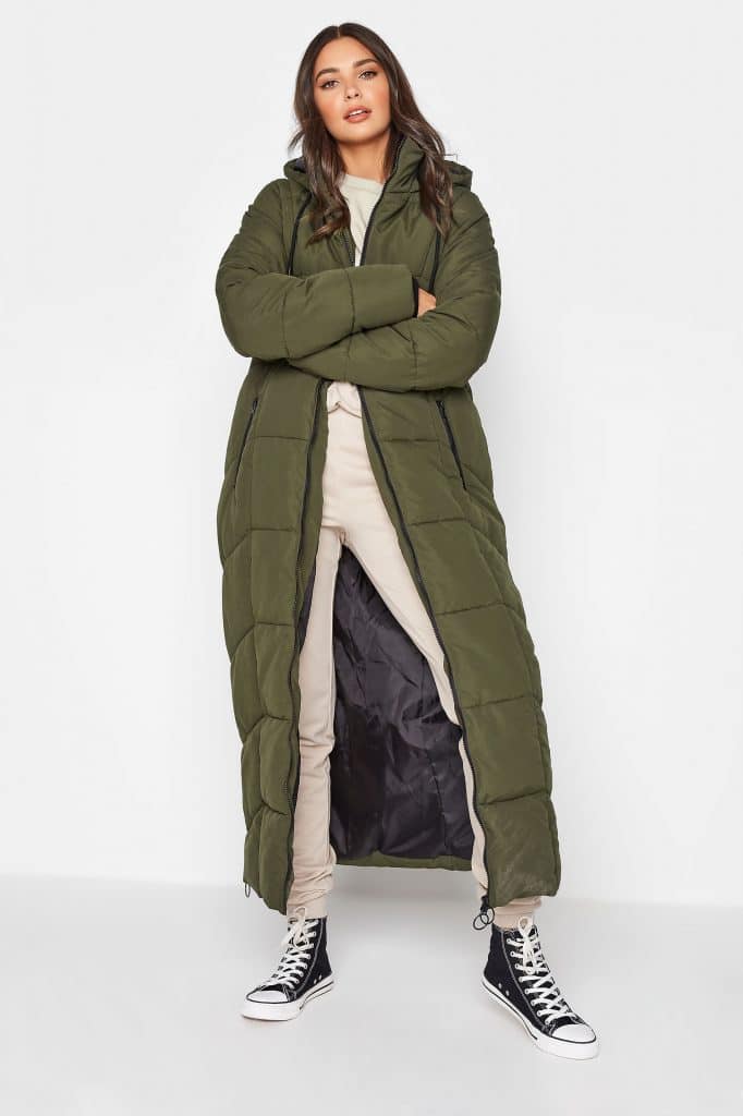 A tall woman in a long olive green quilted puffer coat with extended sleeves.