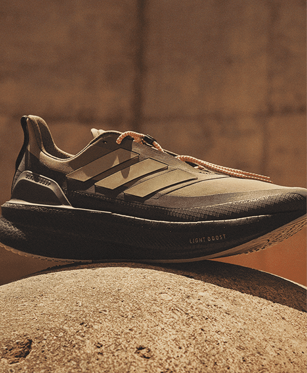 A black and beige Adidas sneaker with bright orange laces on a stone surface.