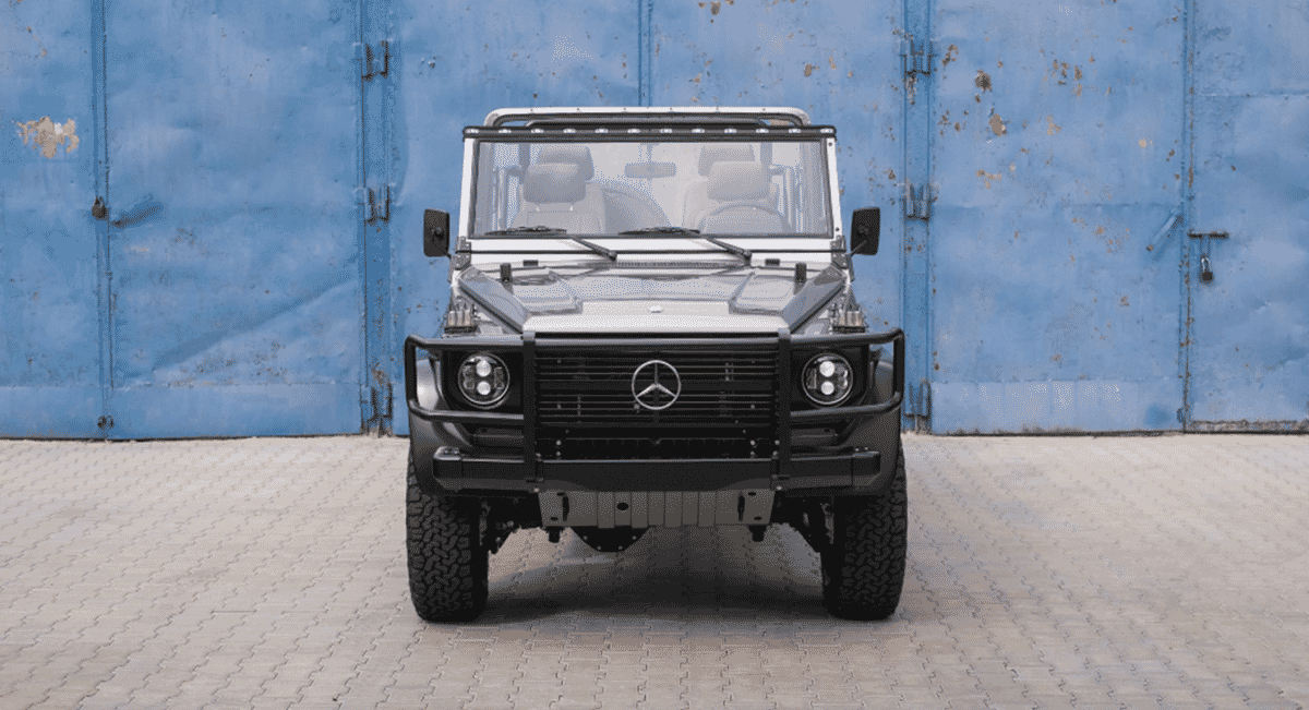 Modified silver Mercedes-Benz G-Wagon parked against a weathered blue wall.