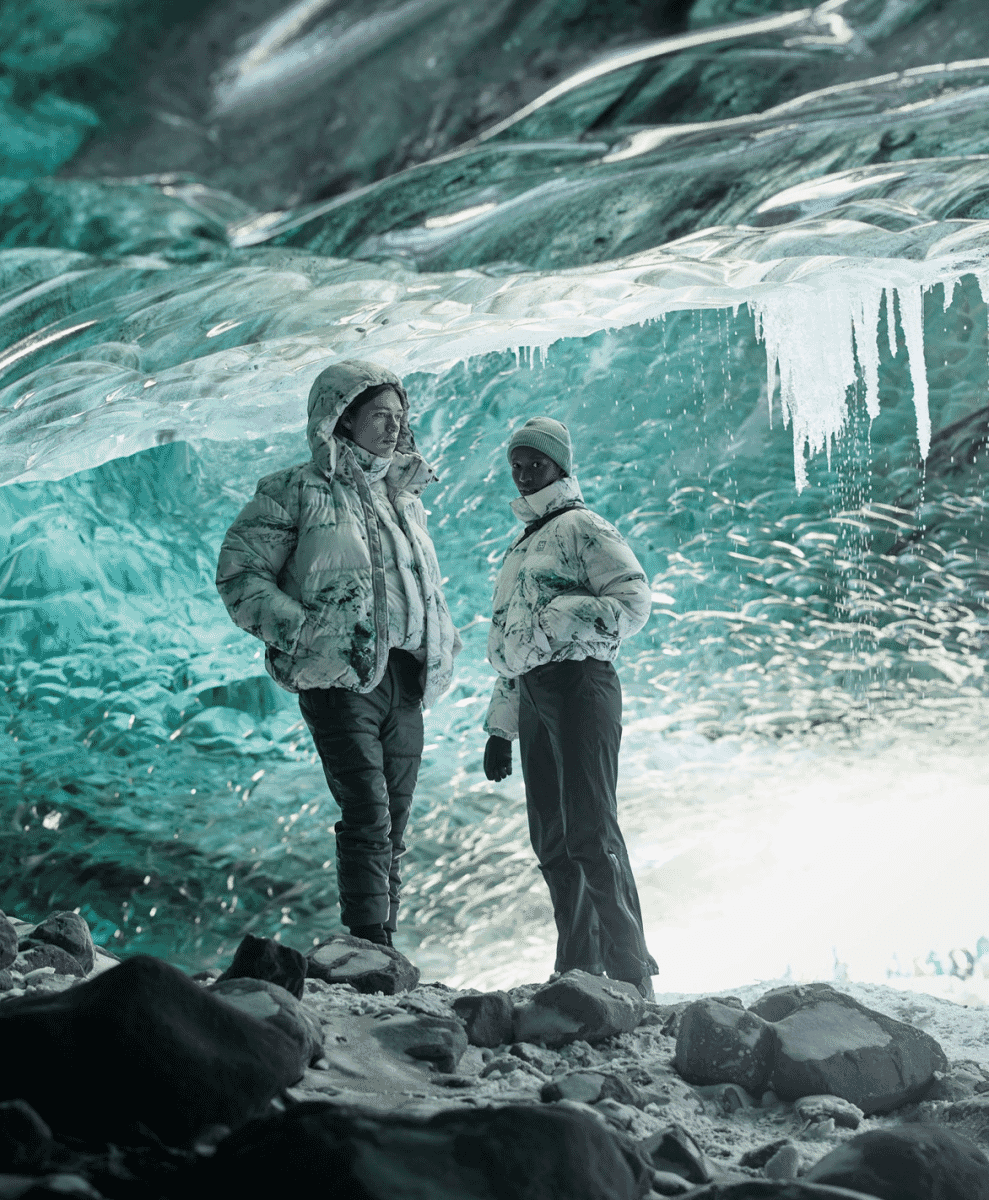Individuals in white puffer jackets exploring a blue ice cave.