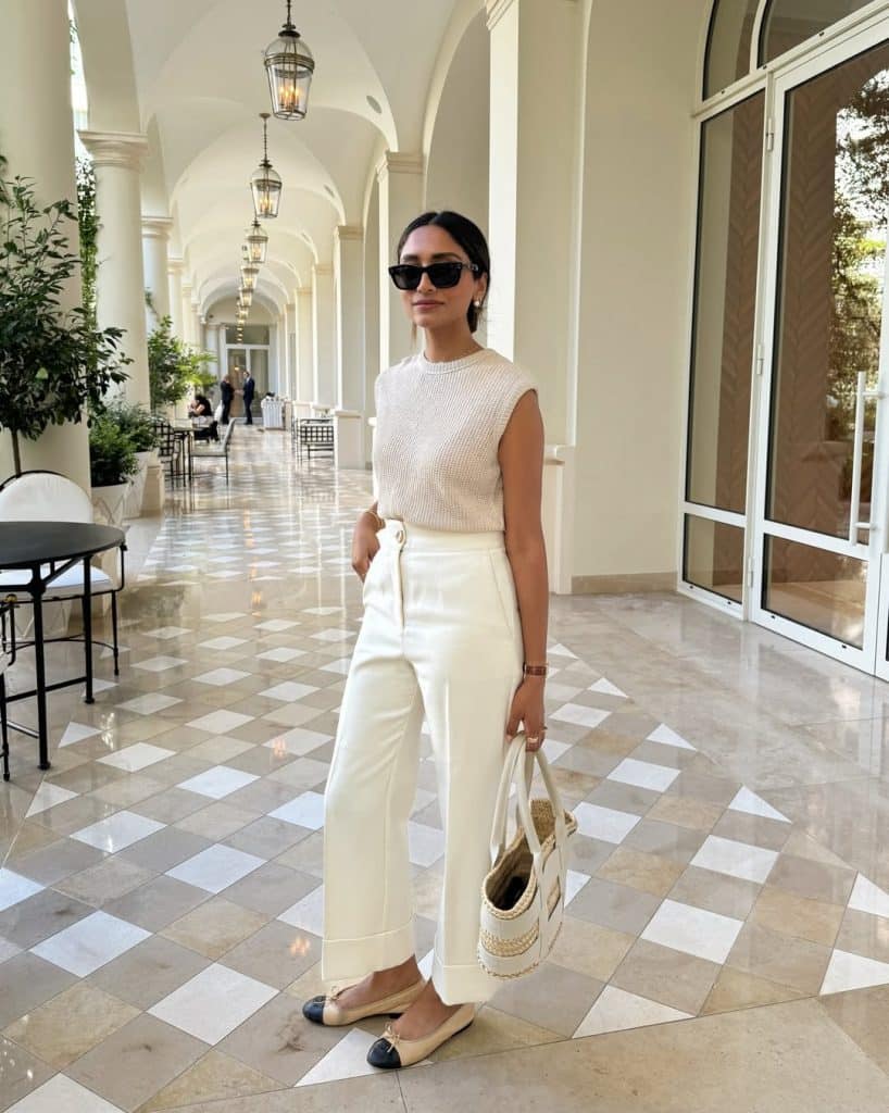 A woman in an all-white knit top and wide-leg trousers in a luxury arched corridor.
