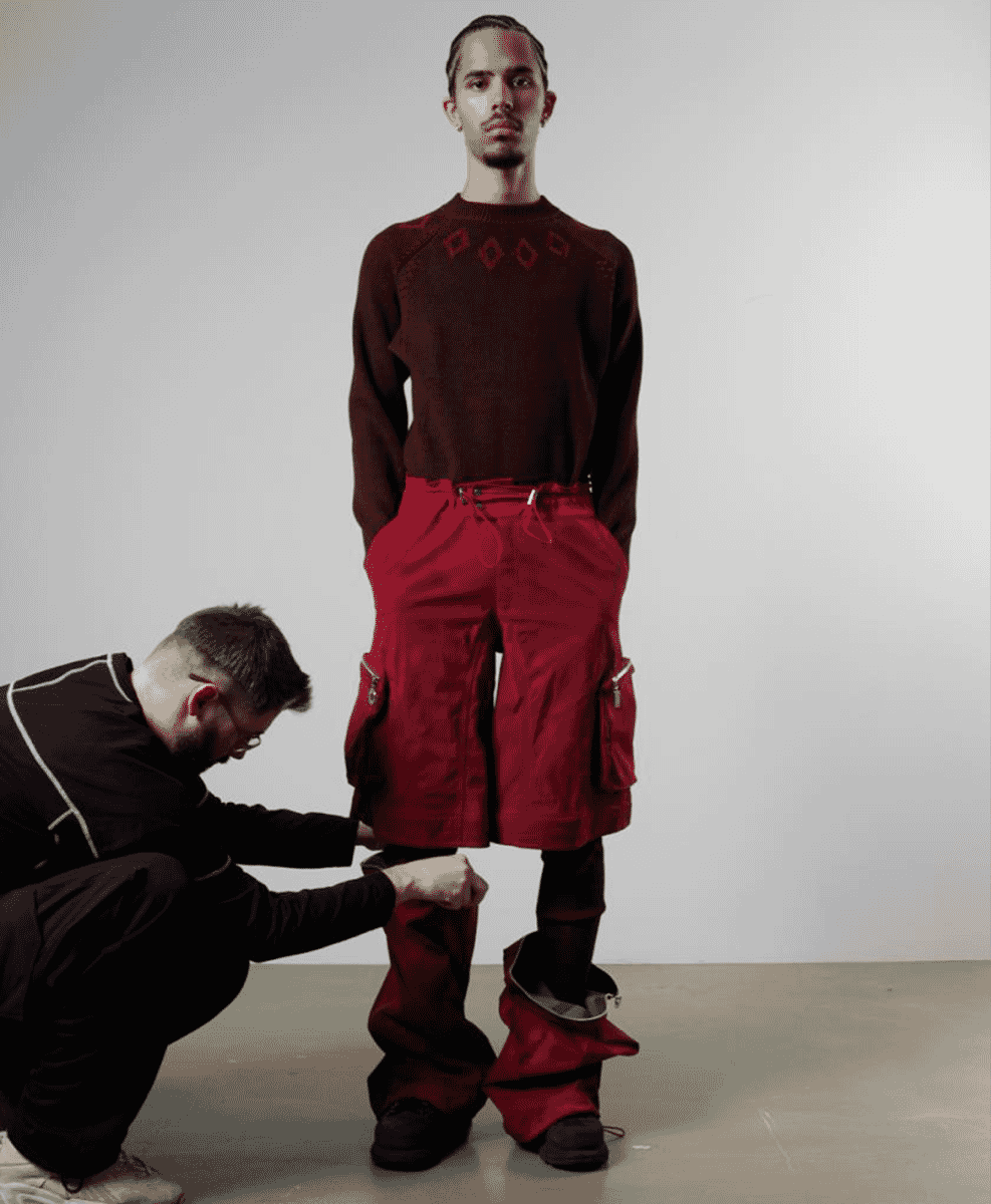A model in an avant-garde diamond-patterned sweater and red shorts in a studio.