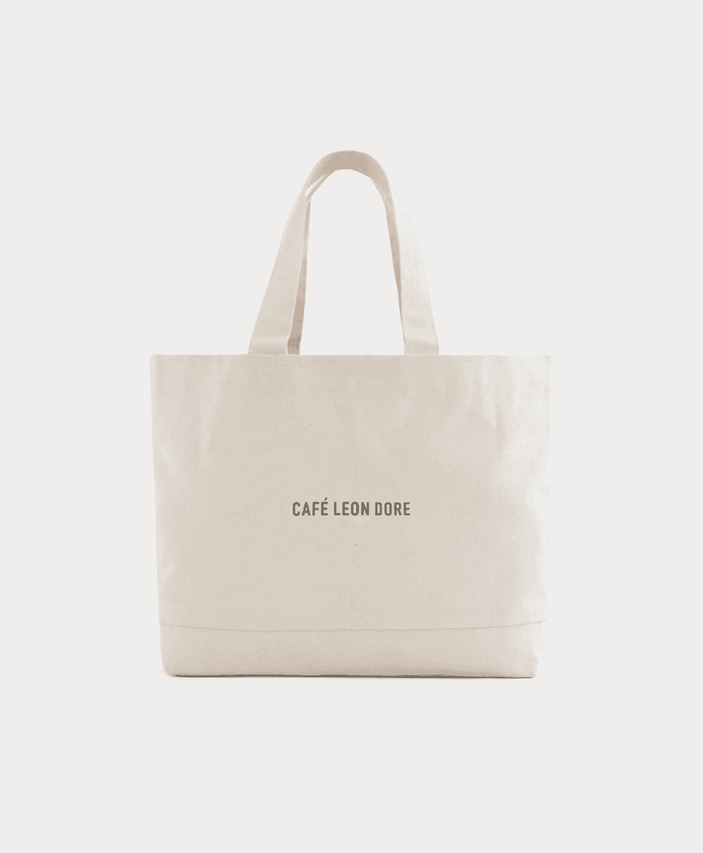 A minimalist cream canvas tote bag with Café Leon Dore branding.
