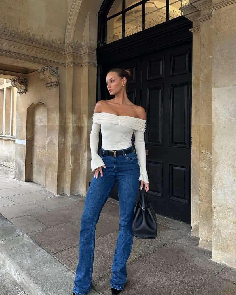 Woman in a white off-shoulder top and high-waisted blue flare jeans.
