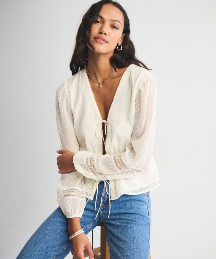 Long-sleeve white top with a tie-front closure and delicate trim.