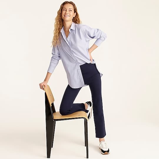 A woman in an oversized light blue shirt and navy trousers in a studio setting.