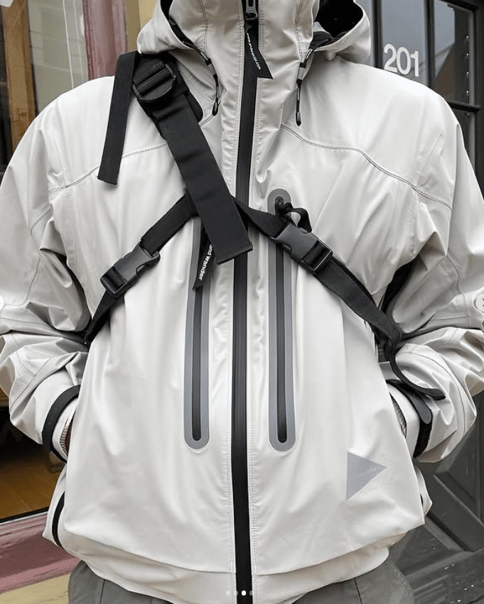 Light gray technical jacket featuring reflective details and black straps.