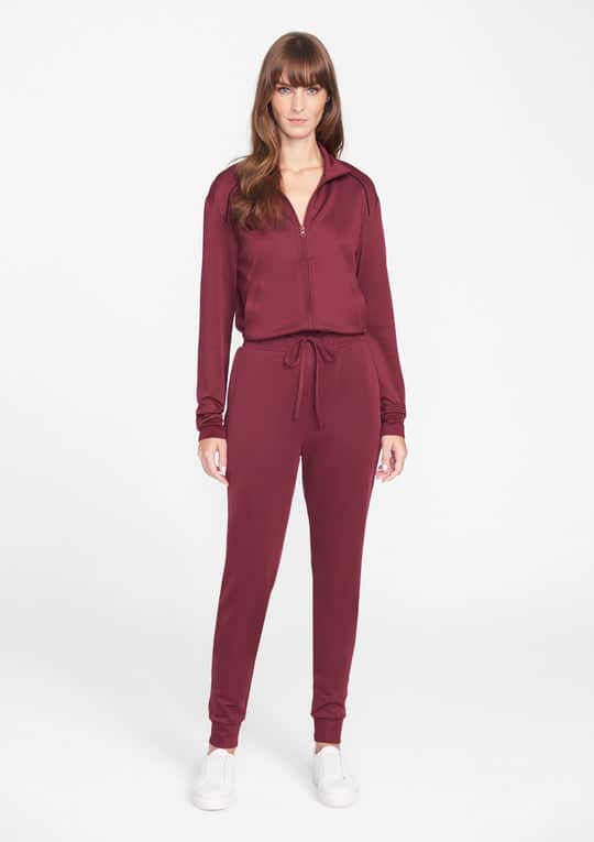 A woman modeling a maroon two-piece jogger set with white sneakers.