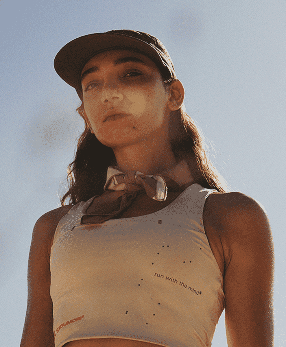 A woman modeling a white cropped tank top with perforated technical fabric and branding.