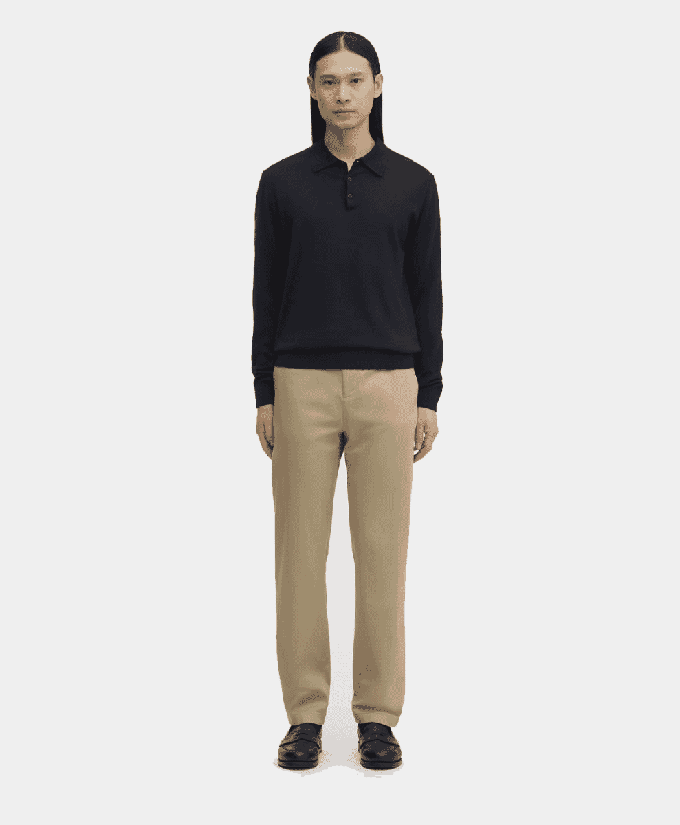 Man in a black long-sleeve polo shirt with beige trousers and black leather shoes.