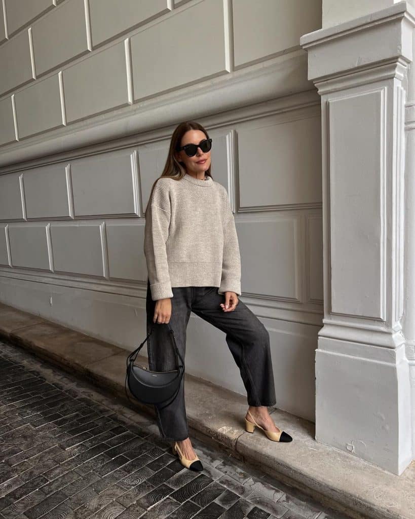 Street style shot of a woman in a beige oversized sweater and dark-wash barrel jeans with two-tone heels.