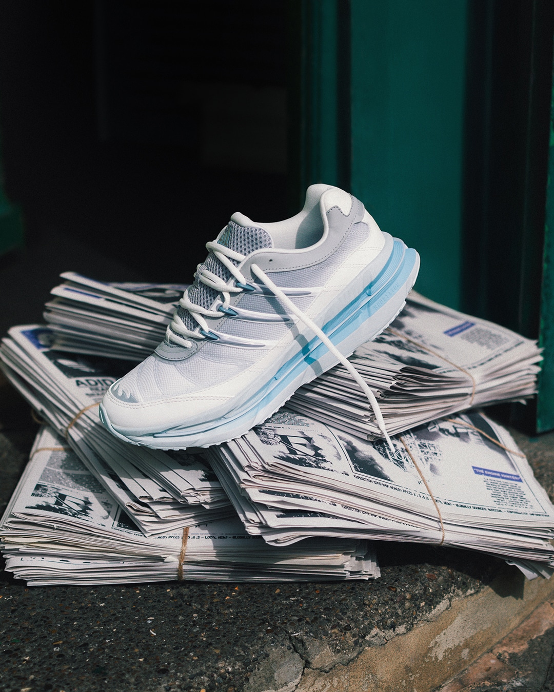 The white and blue adidas sneaker on a bundle of newspapers on a concrete curb.