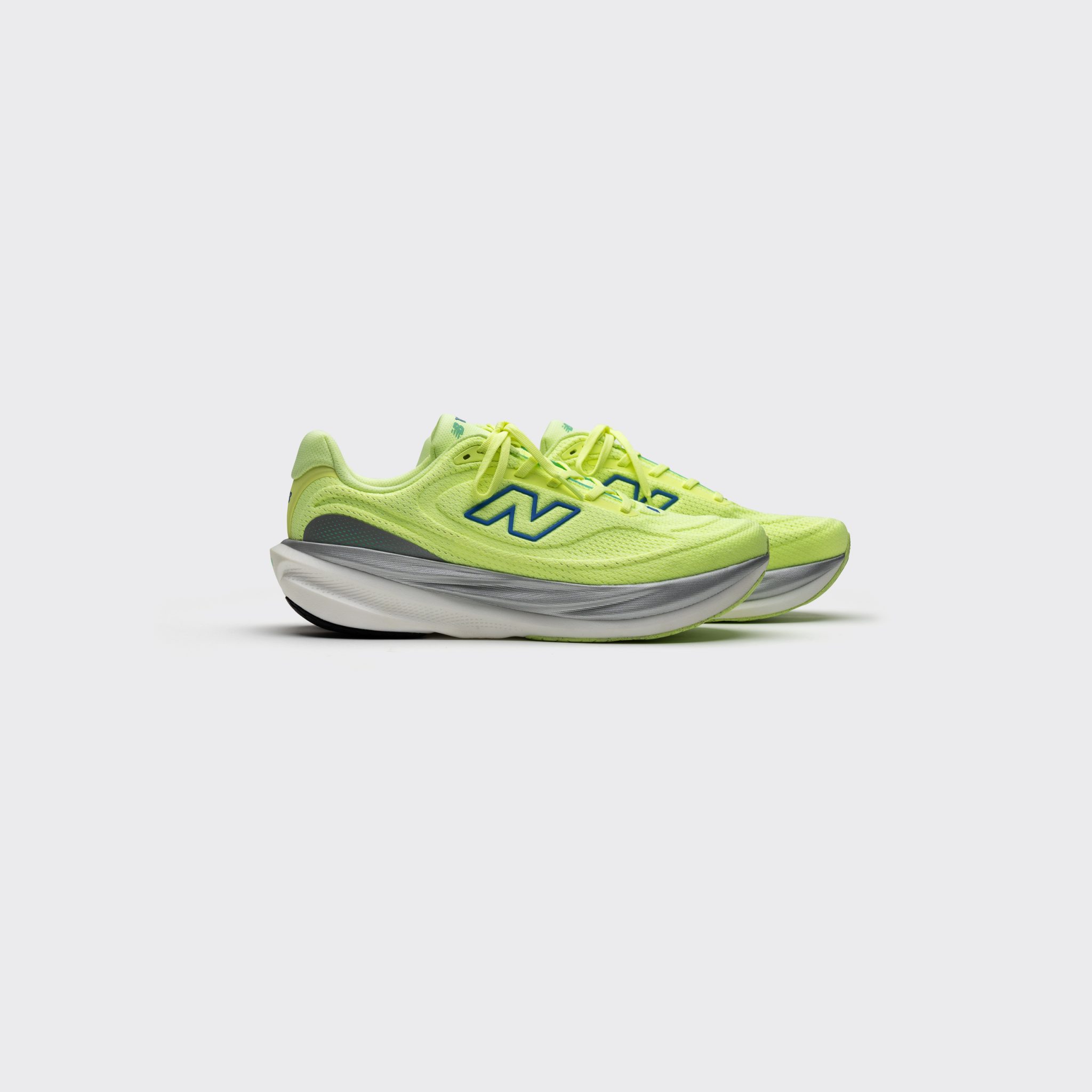Full view of neon yellow New Balance running shoes with blue logo and layered midsole on a white background.