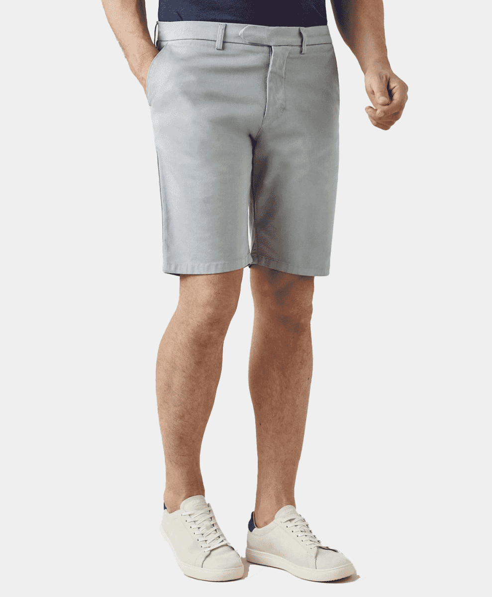 Man wearing light gray chino shorts with a dark blue shirt and white sneakers.