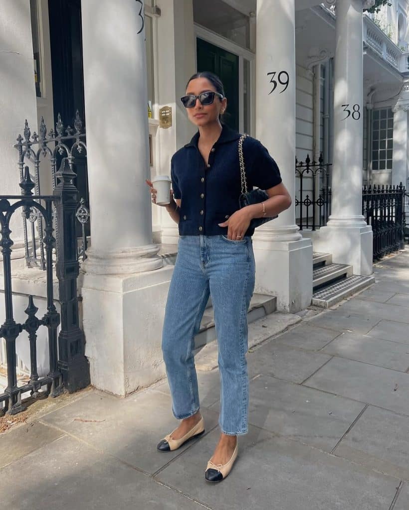Woman in a navy blue button-up cardigan and light-wash jeans walking on a London street.
