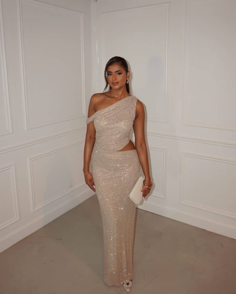 A woman in a champagne one-shoulder sequined gown with a cutout waist.