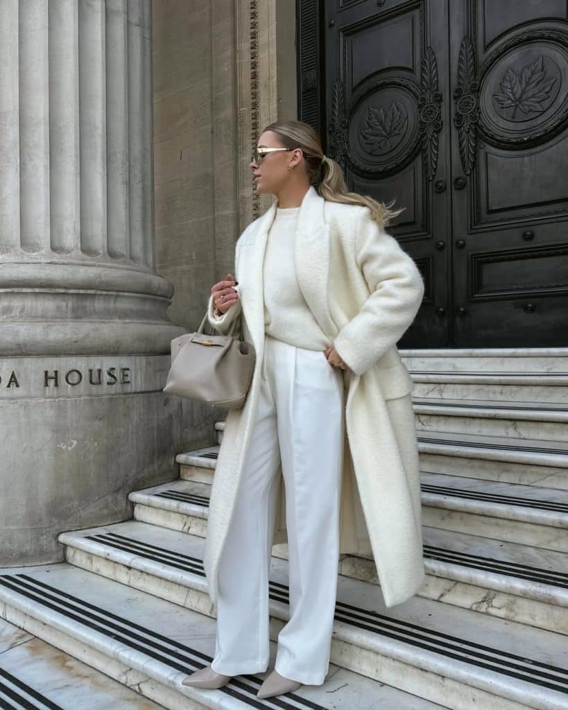 Woman wearing an all-white ensemble with a fluffy coat and wide-leg trousers on marble steps.