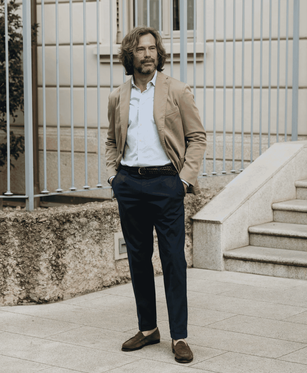 Man wearing a beige blazer over a white shirt with navy trousers and brown loafers.