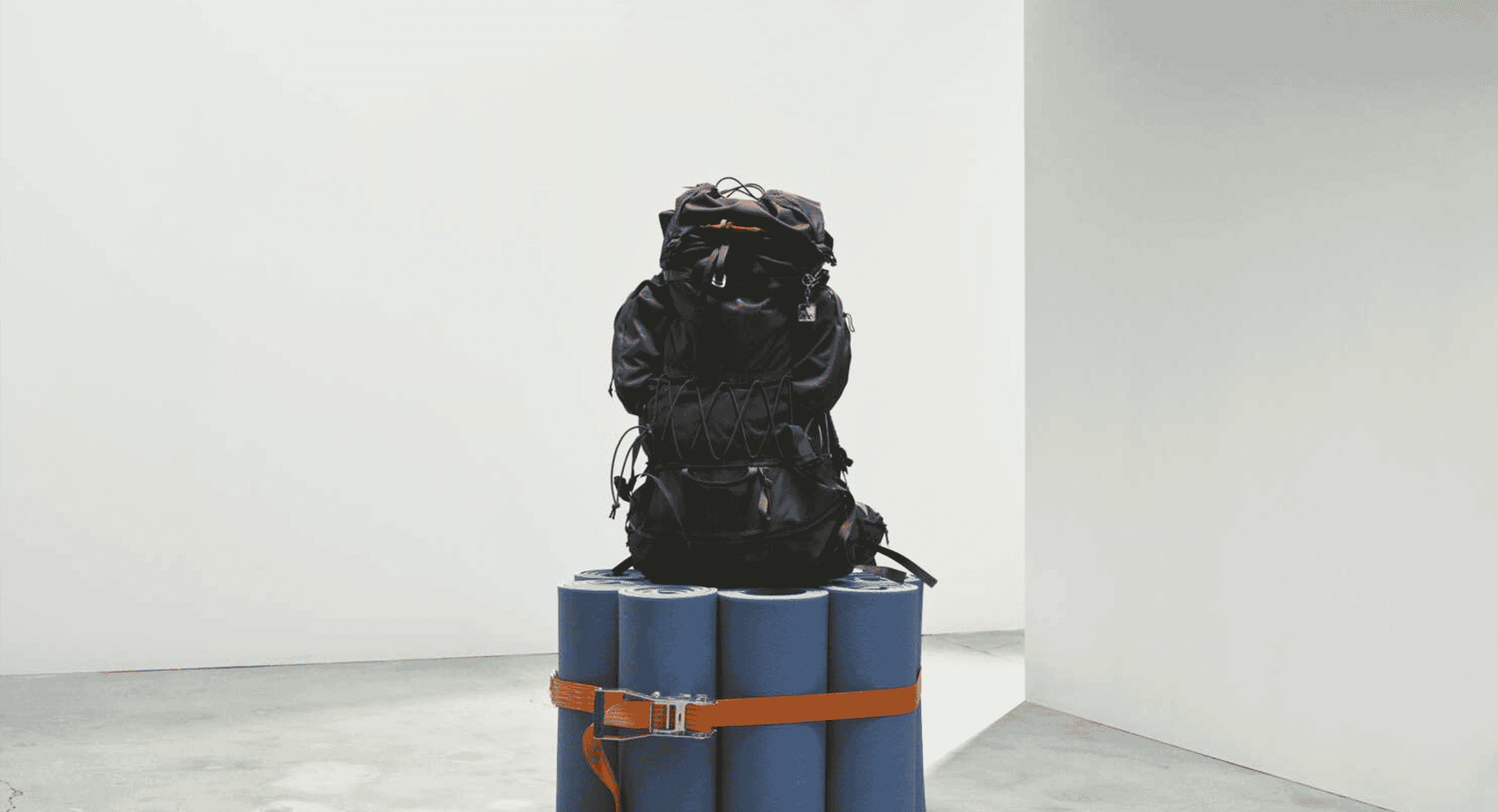 A black technical hiking backpack resting on blue rolled foam mats in a white studio space.