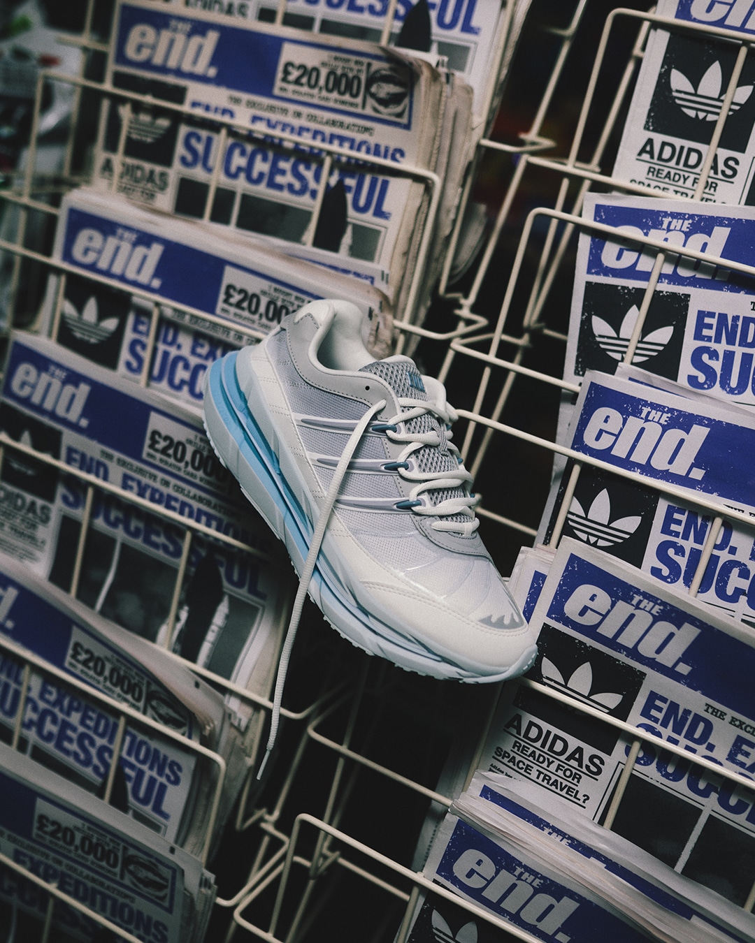 The white and light blue adidas sneaker hanging in a wire newspaper rack.
