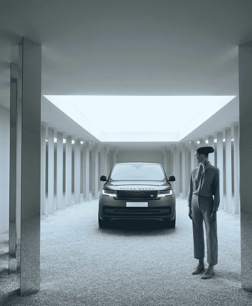Woman in a minimalist grey suit standing beside a modern Range Rover in a white architectural space.