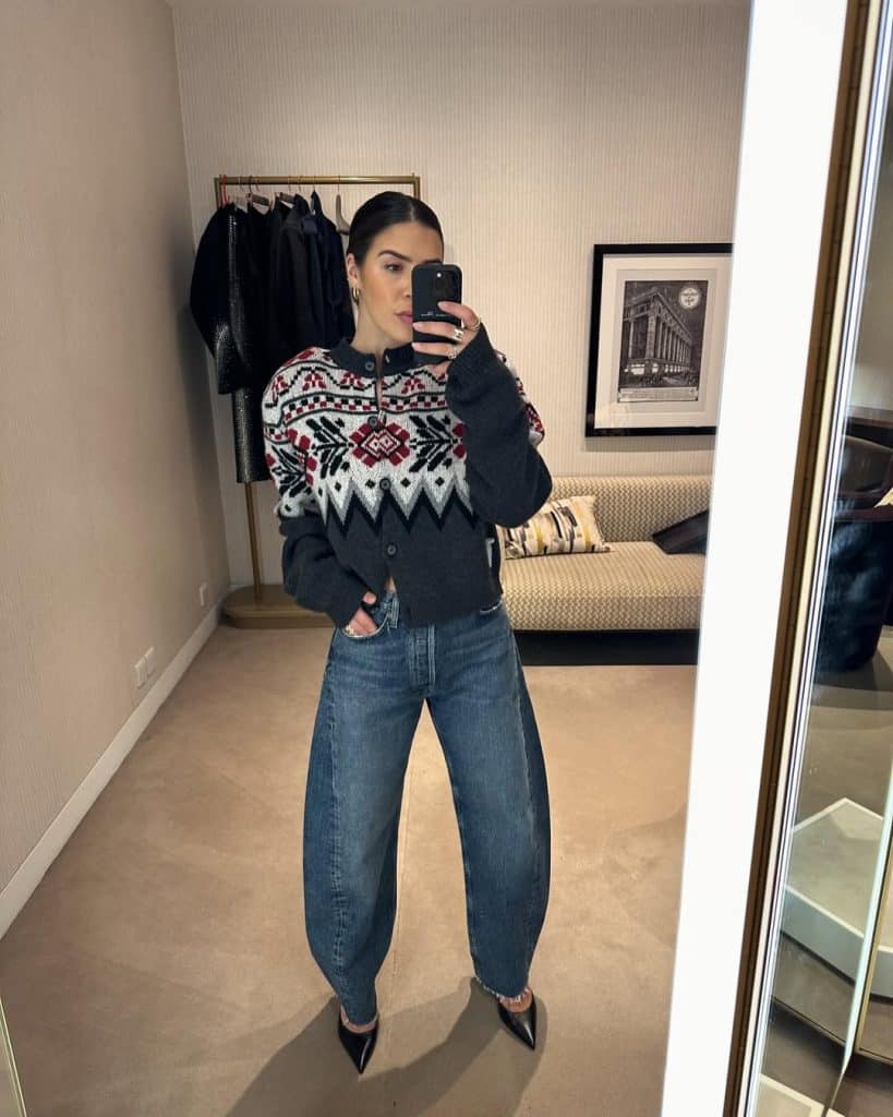 Mirror selfie of a woman in a patterned black, white, and red cardigan with blue barrel jeans.