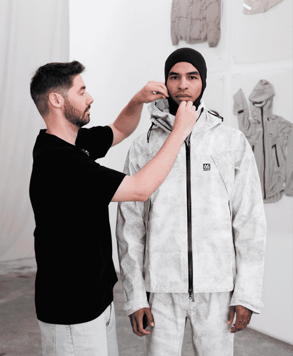 A model in a light gray technical jacket being styled in a minimalist studio.