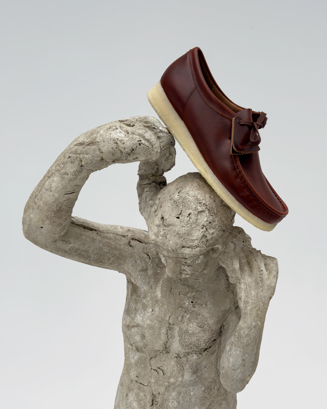 A brown leather loafer resting on a concrete sculpture in a minimalist studio.