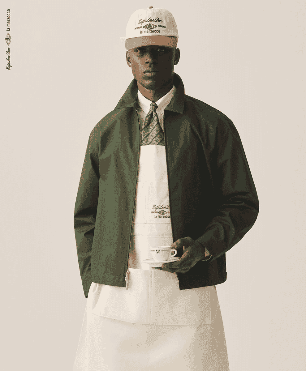 A model wearing an olive green jacket, white apron, and tie from the ALD x La Marzocco collection.