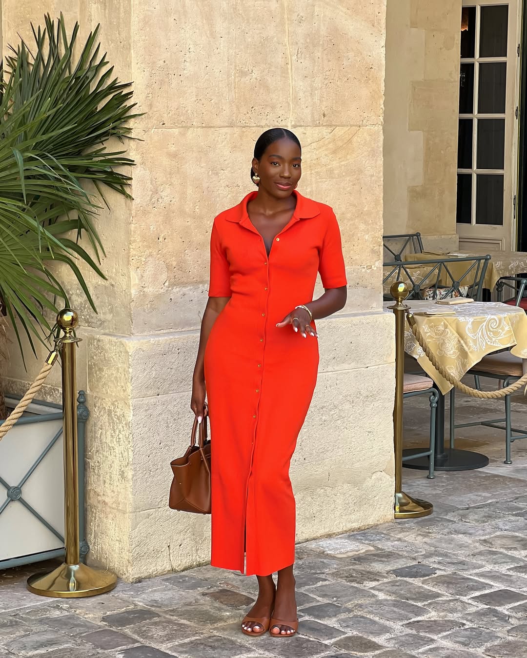 A woman in a vibrant orange button-down midi dress holding a brown tote bag.