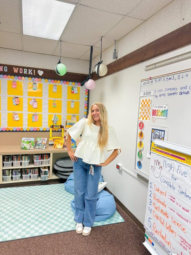 A woman in a white peplum top and blue jeans in a bright classroom.
