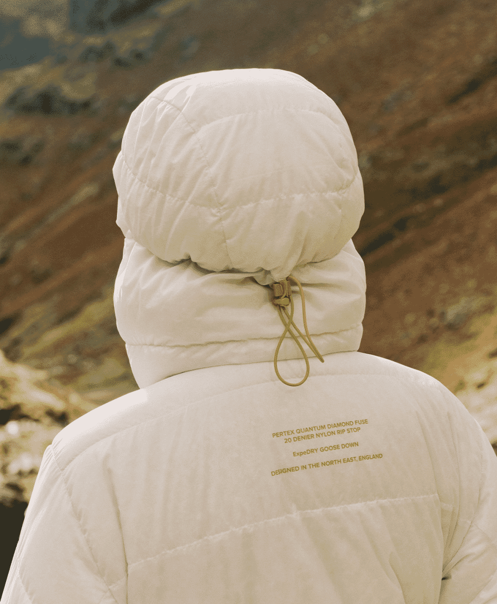 Rear view of a white puffer jacket featuring technical specifications printed on the fabric against a mountain backdrop.