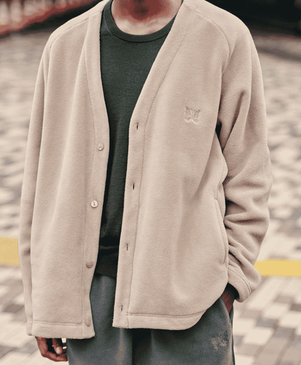 A person wearing a beige fleece cardigan with a chest butterfly embroidery over a green crewneck.