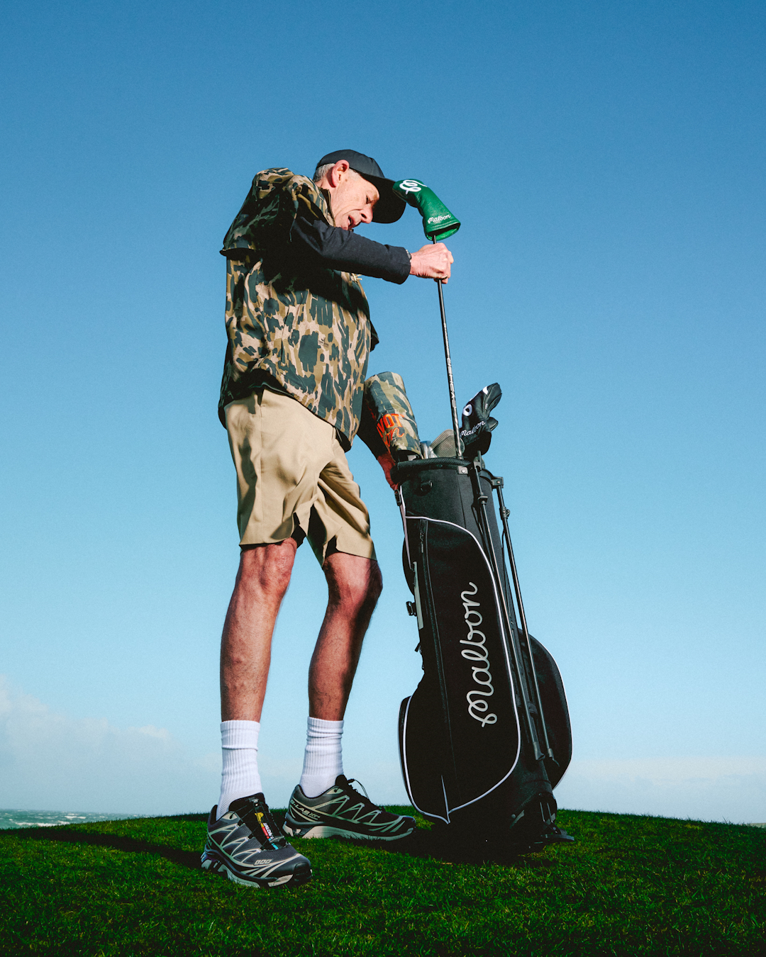 Lifestyle shot of a golfer in mid-swing wearing a Malbon technical vest and oversized trousers.