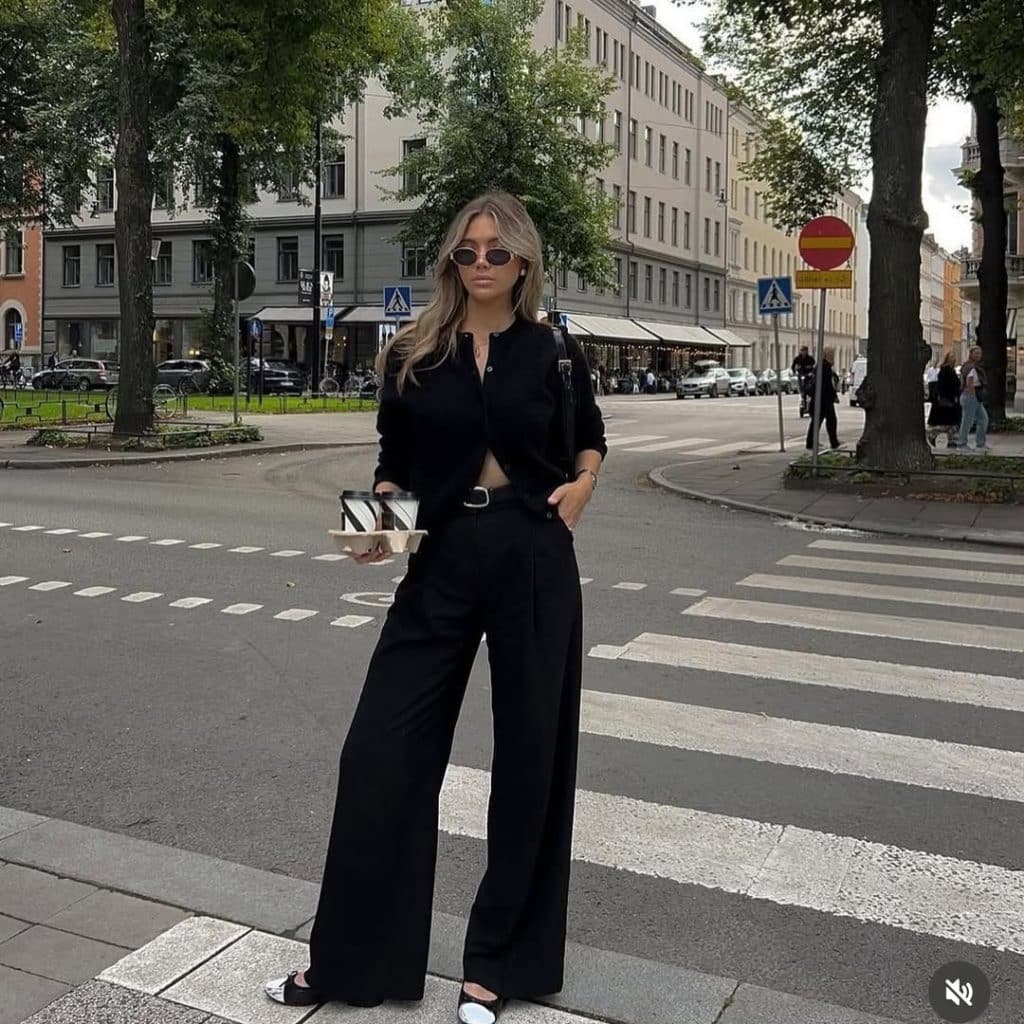 A woman in an all-black outfit featuring a cropped blouse and wide-leg trousers on a city street.
