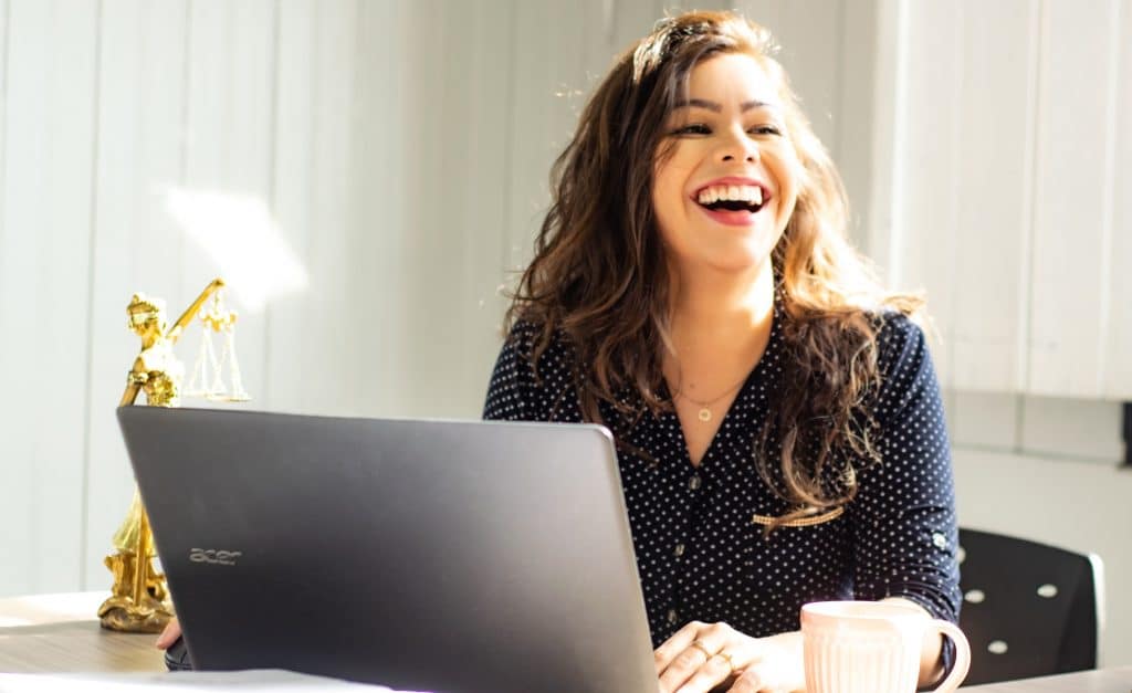 A joyful woman wearing a polka-dot button-up shirt in an office setting, representing polished personal grooming.