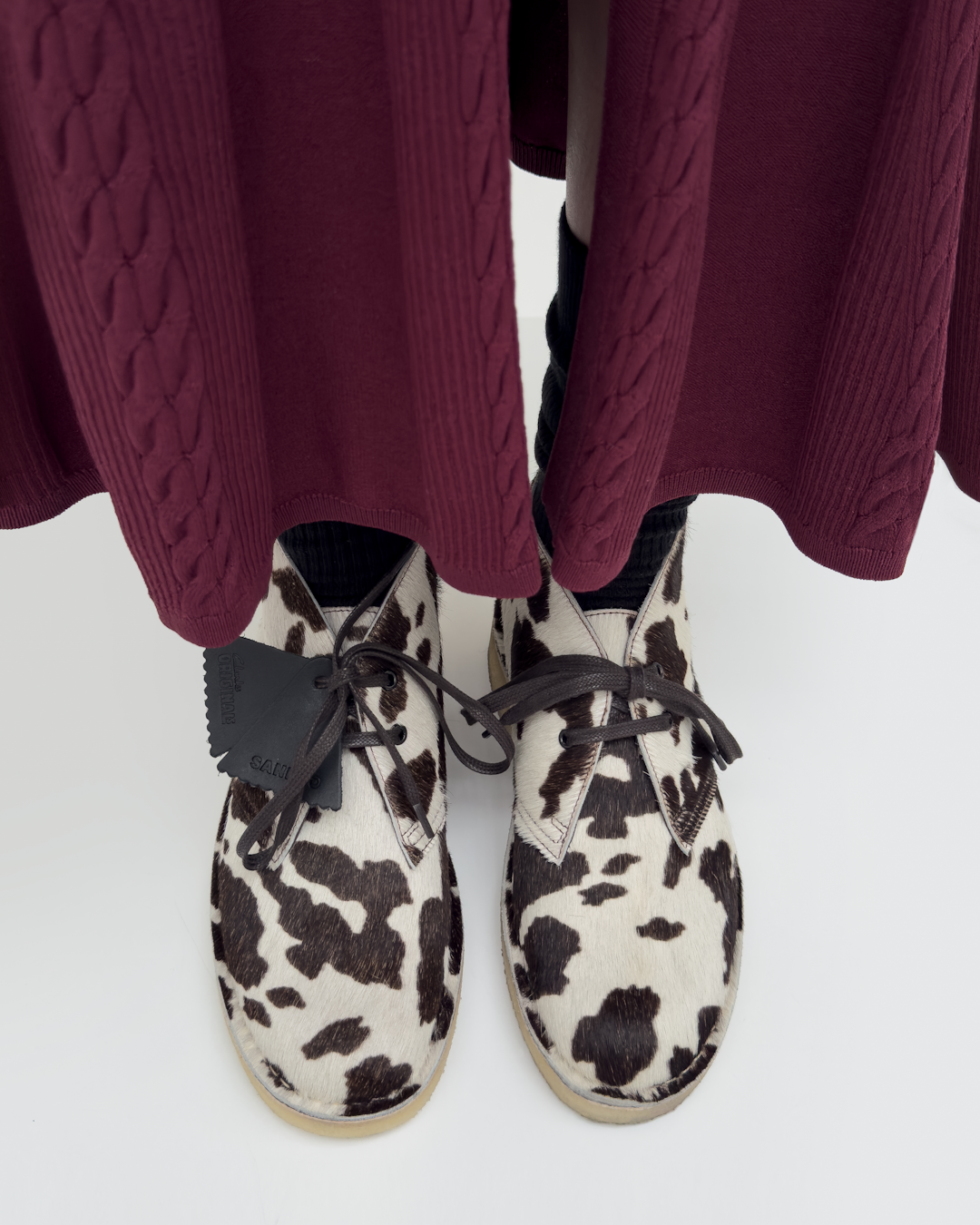 Cow-print Clarks desert boots paired with a maroon cable-knit skirt.